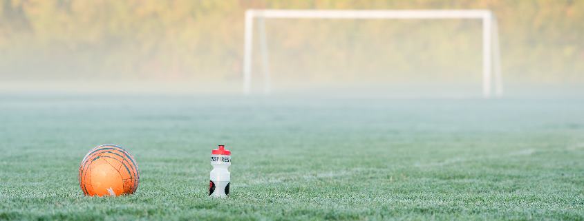 Fussball und Trinkflasche auf Fussballfeld vor leeren Tor im Nebel